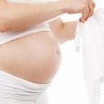 Беременная женщина с оголенным животом держит слип для ребенка